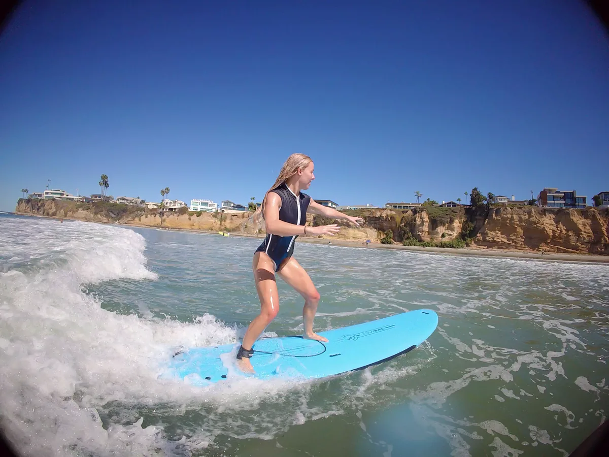 A surfer balancing on a blue board as a small wave breaks behind them