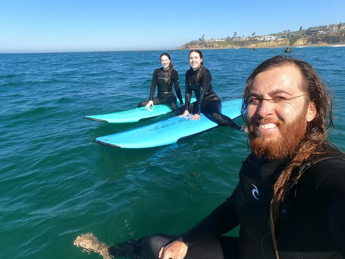 Will Machado smiling in the water with two students and their blue surfboards